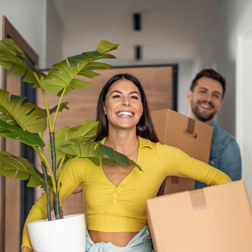 Smiling lady carrying a plant ready to move into her new apartment after a successful apartment inspection.